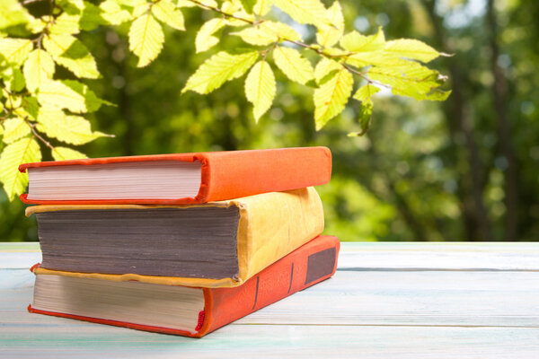 Stack of colorful books on wooden table on natural blurred background. Back to school. Copy space