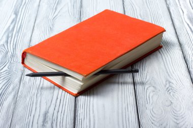 Blank red hardcover book with black pencil on white wooden background.