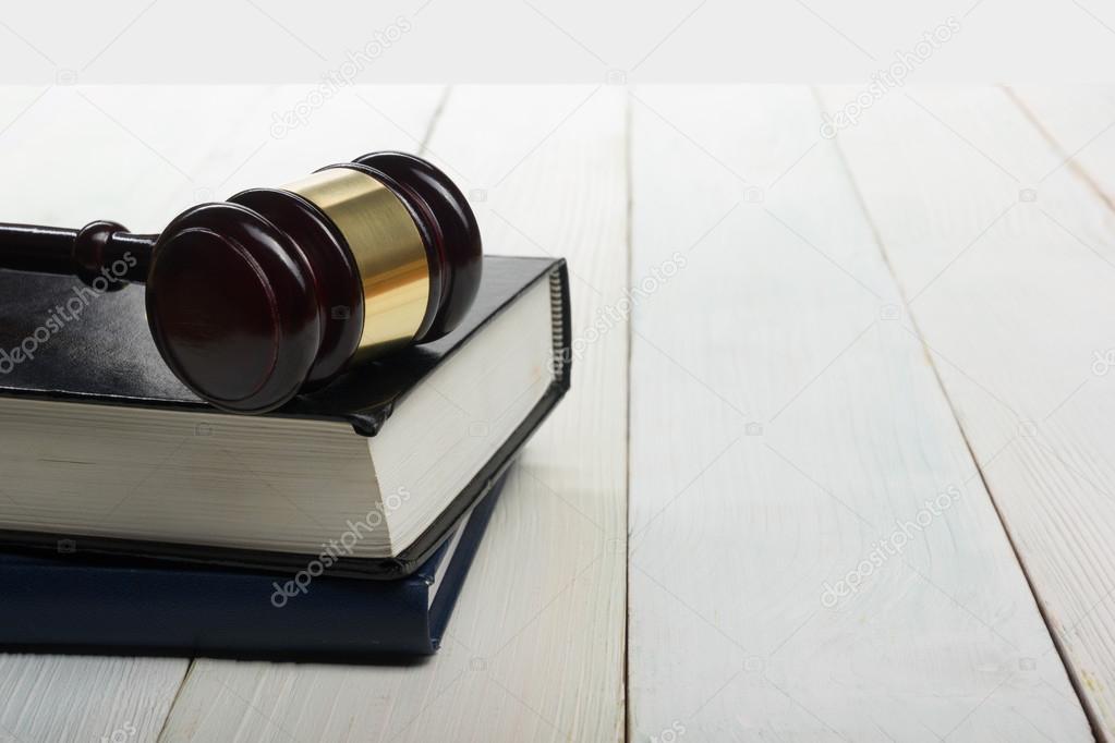 Open law book with wooden judges gavel on table in a courtroom