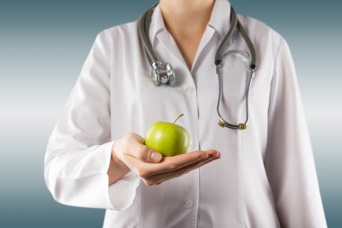 Female doctors hand holding green apple. Close up shot on grey