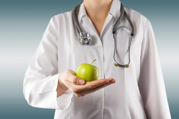 Female doctors hand holding green apple. Close up shot on grey — Stok fotoğraf