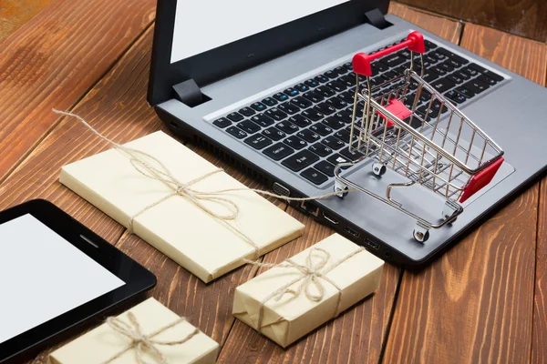 Concepto de compras en línea - Carro de compras vacío, ordenador portátil y tableta pc, caja de regalo sobre fondo de madera rústico — Foto de Stock