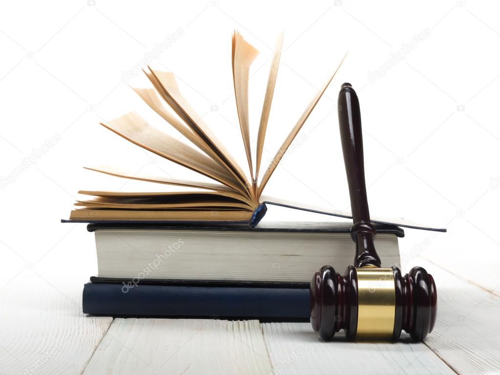 Open law book with wooden judges gavel on table in a courtroom