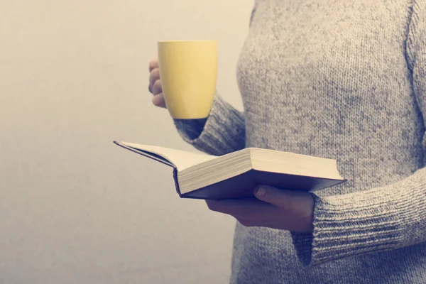 Jonge vrouw lezen van een boek en houden kopje thee of koffie. Getinte afbeelding — Stockfoto