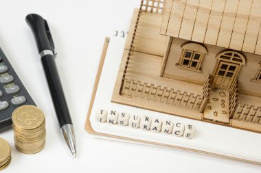 Konut satın alma ve sigorta kavramı. Ofis resepsiyon masası malzemeleri en iyi manzaralı. Hesap makinesi. altın sikke, kalem, not defteri, yeşil model evi, ahşap blok kelime
