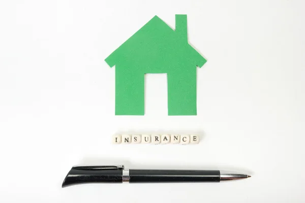Concept of housing purchase and insurance. Office desk table with supplies top view - pen, green model house, wooden block with word Insurance. — 图库照片