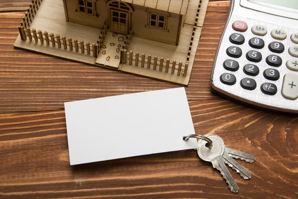 Concepto de Bienes Raíces. Casa modelo, llaves, tarjeta de visita en blanco, bolígrafo y calculadora en mesa de madera. Vista superior . — Foto de Stock