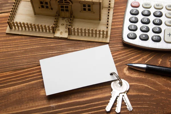 Real Estate koncept. Model domu, klíče, prázdná vizitka, pero a Kalkulačka na dřevěný stůl. Pohled shora. — Stock fotografie