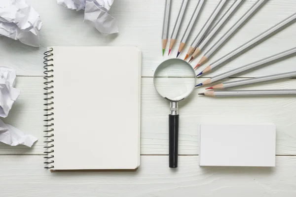 Zerknüllte Papierkugeln, Lupen, Bleistifte und Notizbuch mit weißem Blatt auf dem Holztisch. Konzept zur Kreativitätskrise — Stockfoto