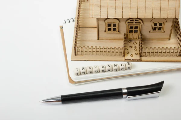 Concept of housing purchase and insurance. Office desk table with supplies top view. Pen, notepad, model house, wooden block word Royalty Free Φωτογραφίες Αρχείου