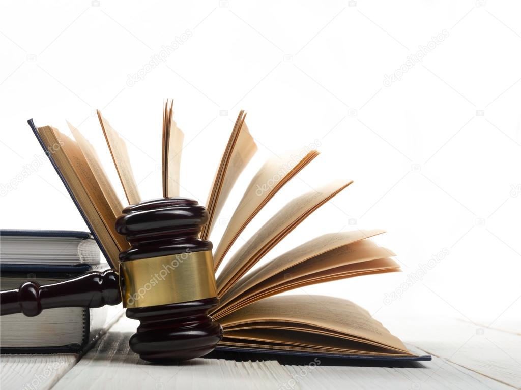 Open law book with wooden judges gavel on table in a courtroom