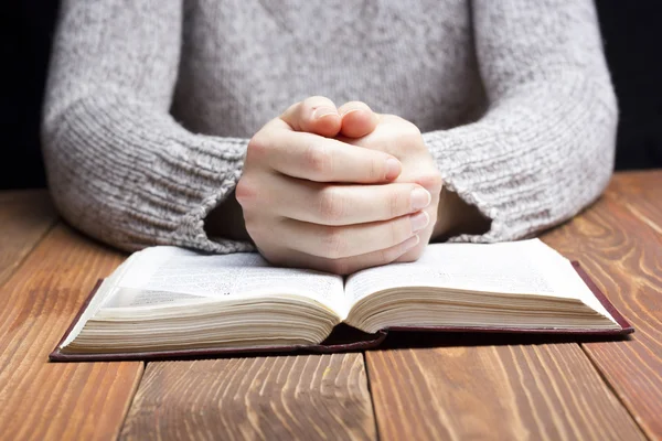 Mani di donna che pregano con una bibbia al buio sul tavolo di legno — Foto Stock