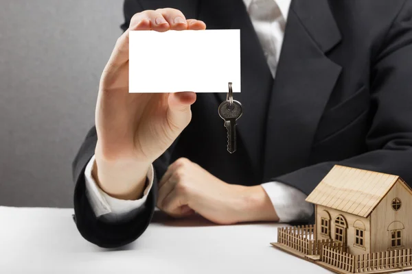Concepto inmobiliario. Agente Manos sosteniendo tarjeta de visita en blanco con llaves . — Foto de Stock