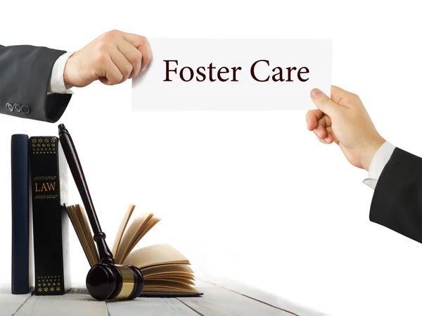 Βιβλίο νόμου και δικαστές ξύλινο σφυρί στο τραπέζι σε μια αίθουσα του Δικαστηρίου ή του νόμου υπηρεσία αναγκαστικής εκτέλεσης. Δικηγόρος χέρια που κρατούν την επαγγελματική κάρτα με κείμενο Foster Care — Φωτογραφία Αρχείου
