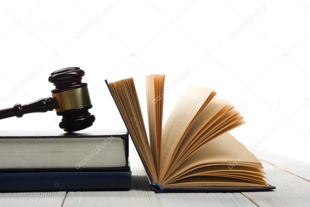 Open law book with wooden judges gavel on table in a courtroom