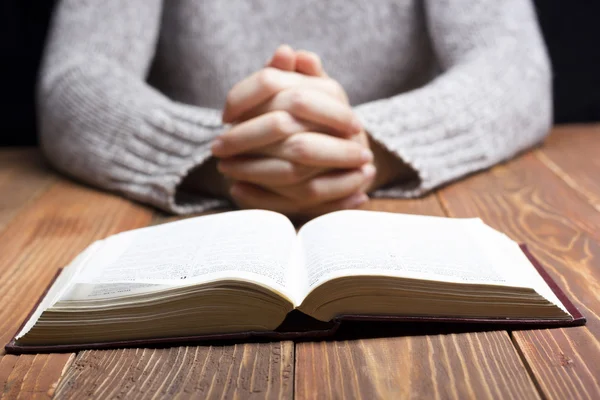 Manos de mujer rezando con una Biblia oscura sobre mesa de madera — Foto de Stock