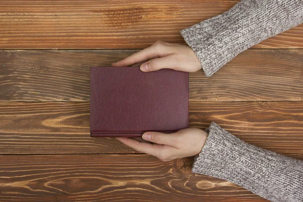 Female hands hold a blank empty book or note, diary cover on the wood desk table, top view — Stock Photo, Image