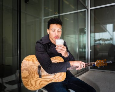 Sokakta gitar ve bir fincan kahveyle oturan yakışıklı genç adam - sokak müzisyeni, kampüs dışı hayatı, kış ya da bahar tatili