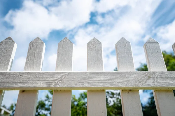 White picket fence under a blue sky in the summer reaching for heaven