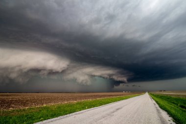 Dangerous storm with shelf cloud approaches quickly over a farm field along a country road. clipart