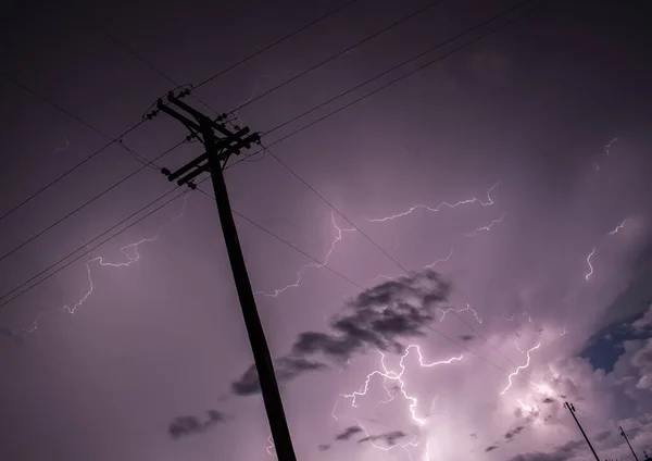 A powerful storm fills the night sky with lightning bolts, behind the silhouette of power lines.