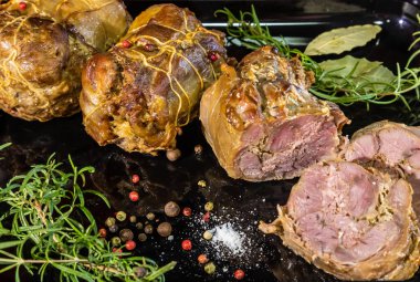 Fırında pişirilmiş et yemeği, arka planda baharat ve biberiye ile süslenmiş.