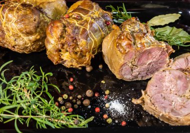 Fırında pişirilmiş et yemeği, arka planda baharat ve biberiye ile süslenmiş.