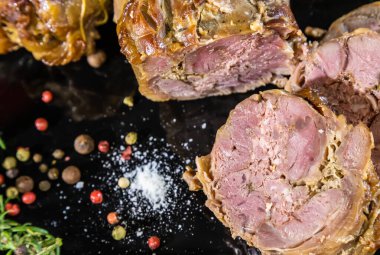 Fırında pişirilmiş et yemeği, arka planda baharat ve biberiye ile süslenmiş.