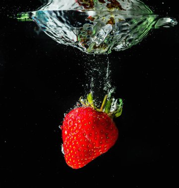 Olgun çilekler suya düşer, sıçramalar ve hava kabarcıkları yükselir.