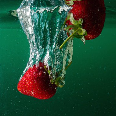 Olgun çilekler suya düşer, sıçramalar ve hava kabarcıkları yükselir.