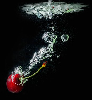 Olgun kirazlar suya düşer, su sıçratır ve hava kabarcıkları oluşur.