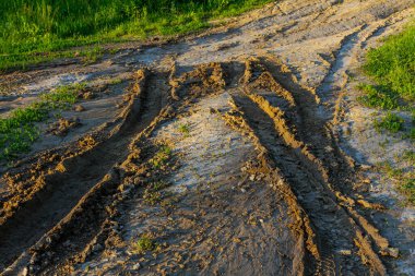 Çamur yolu, altın saat boyunca kırsal alanda lastik izleri ile işaretlenmiş. Bu da doğanın araç hareketinin dokusunu ve etkilerini gözler önüne seriyor..