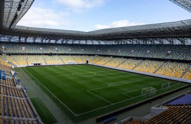 Lviv Oblastı 'nda geniş bir stadyum, açık mavi gökyüzünün altında renkli koltuklarla çevrili boş bir futbol sahası ve huzurlu bir günü gösteren bulutlarla çevrili..