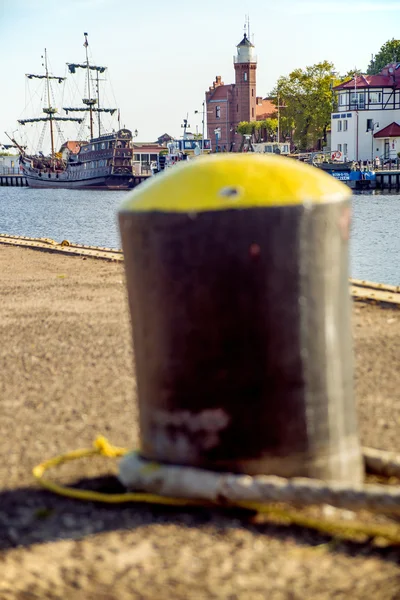 Bolardo en un puerto con barco de vela y faro — Foto de Stock