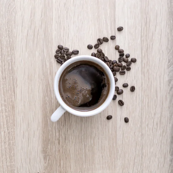 Cangkir kopi dengan biji kopi panggang dengan latar belakang kayu . — Stok Foto