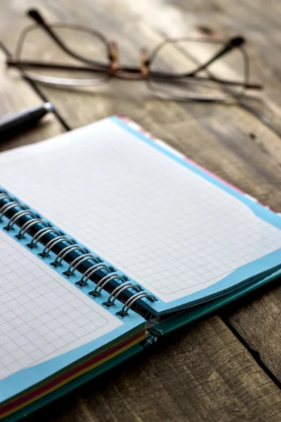 Spiraal gecontroleerd notebook en bril op de achtergrond — Stockfoto