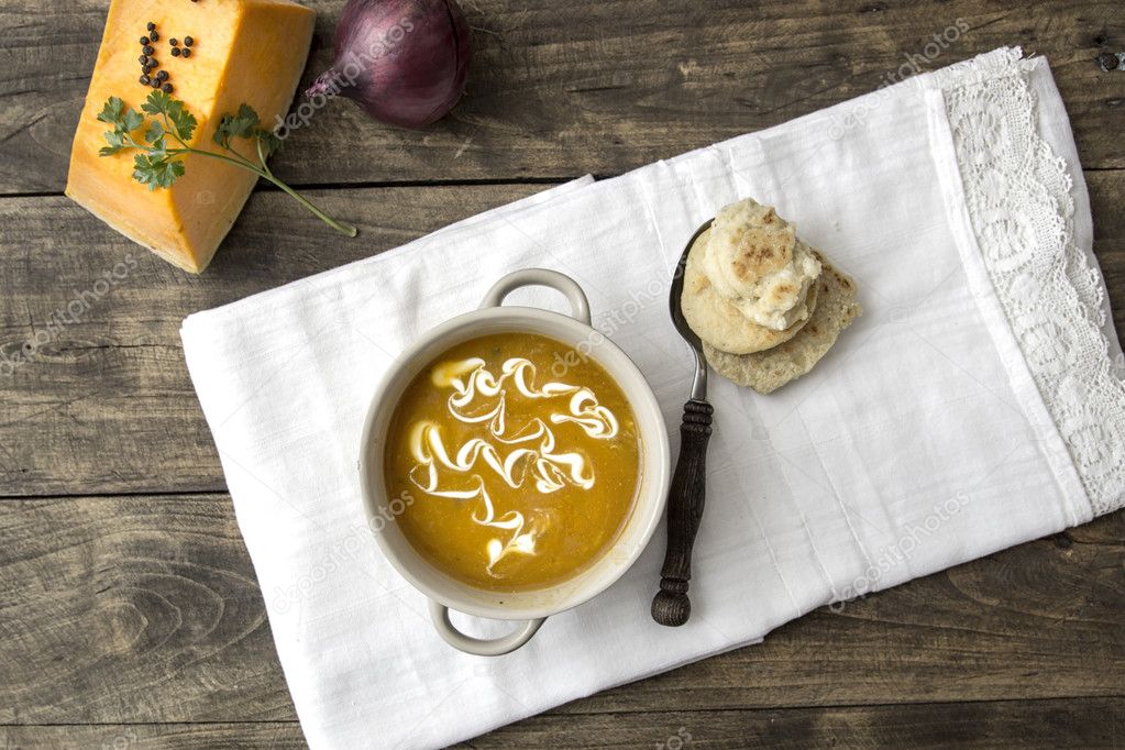 Bowl of hot pumpkin soup with cream on wooden table