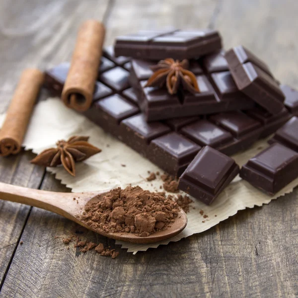 Broken chocolate bar and spices on wooden table. — Stock Photo, Image