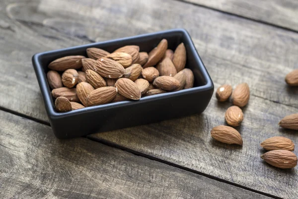 Almonds in  bowl on grained wood background — Stock Photo, Image