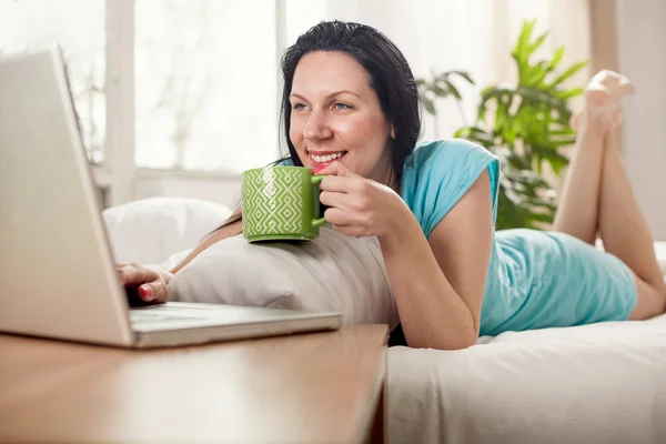 Schöne junge Frau, die mit einer Tasse Kaffee im Bett liegt — Stockfoto