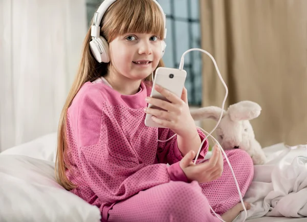 Pequeña chica sonriente escucha música en la cama — Foto de Stock