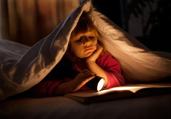 Genç bir kız bir el feneri ile yorganın altında bir kitap okuma — Stok fotoğraf