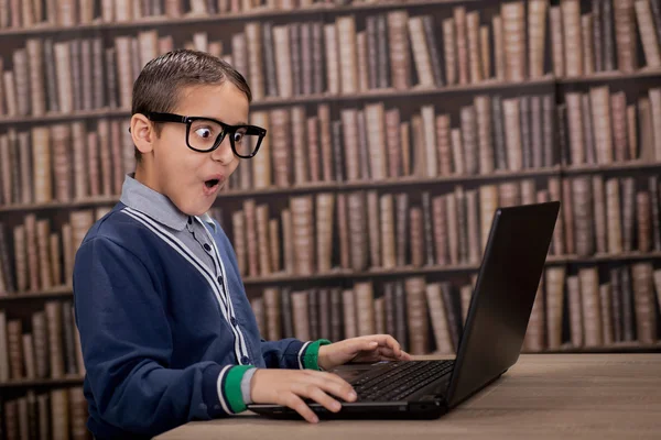 Menino surpreso na biblioteca com computador — Fotografia de Stock