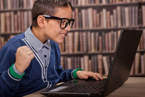 Menino na biblioteca com óculos trabalhando no laptop — Fotografia de Stock