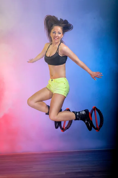 Fit legs in kangoo jumping shoes. Beautiful and sexy girl do sport kangoo  exercises on pink background and sit Stock Photo