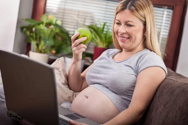 Беременная женщина с помощью ноутбука и прослушивания музыки — стоковое фото
