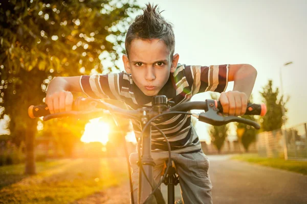 Boy ride a bicycle in city park on sunset — Stock Photo, Image