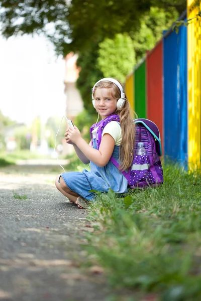젊은 여 자가 다음 학교 울타리에 앉아 음악을 듣고 — 스톡 사진
