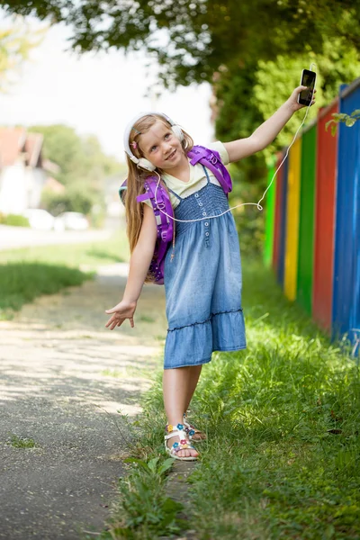 Szczęśliwy, że dziewczynka idzie do szkoły i słuchać muzyki przez smartph — Zdjęcie stockowe