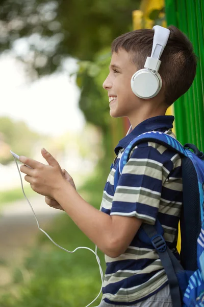 Skolan pojke står nästa på staket och lyssna på musik via sm — Stockfoto